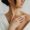 Woman applying moisturizer to her shoulder, showcasing smooth, healthy skin while wrapped in a cozy bathrobe.